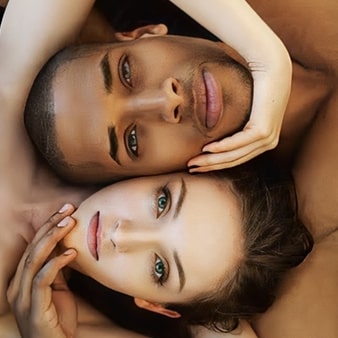 Blonde lady with a black man touching each other chin